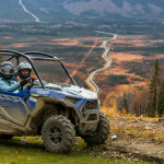 Two riders on UTV's surrounded by fall foliage.
