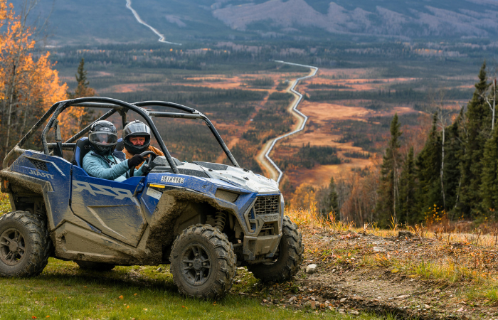 Two riders on UTV's surrounded by fall foliage.