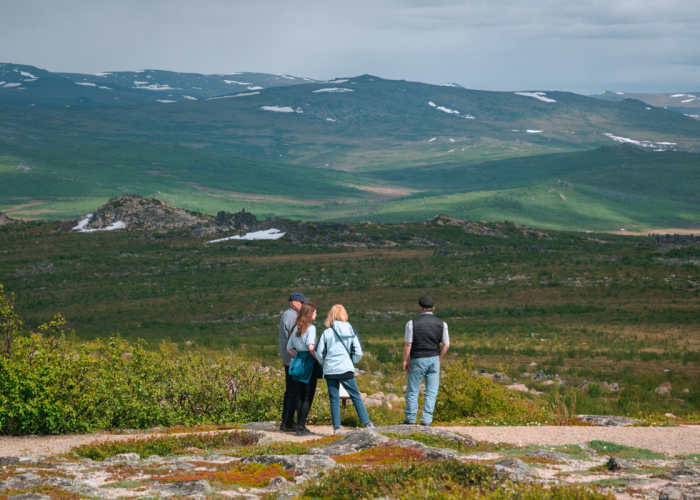 FAMILY LOOKING OUT TO ALASKAN BACK COUNTRY WITH MOUNTAIN RANGE IN DISTANCE