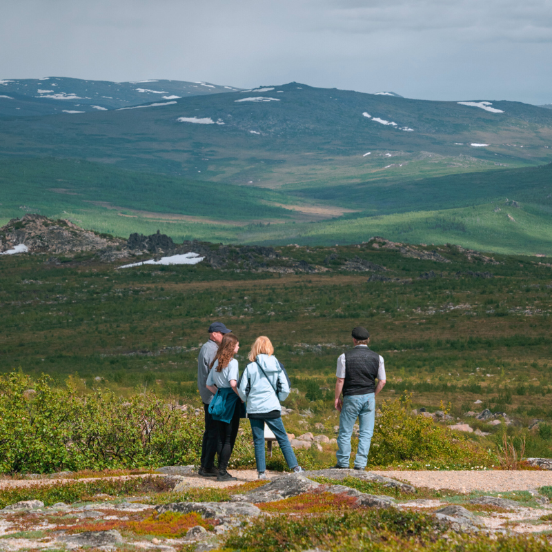 FAMILY LOOKING OUT TO ALASKAN BACK COUNTRY WITH MOUNTAIN RANGE IN DISTANCE
