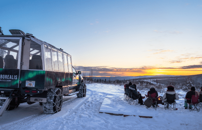 Guests enjoying a campfire as the sun sets on the snowcoach sunset tour.