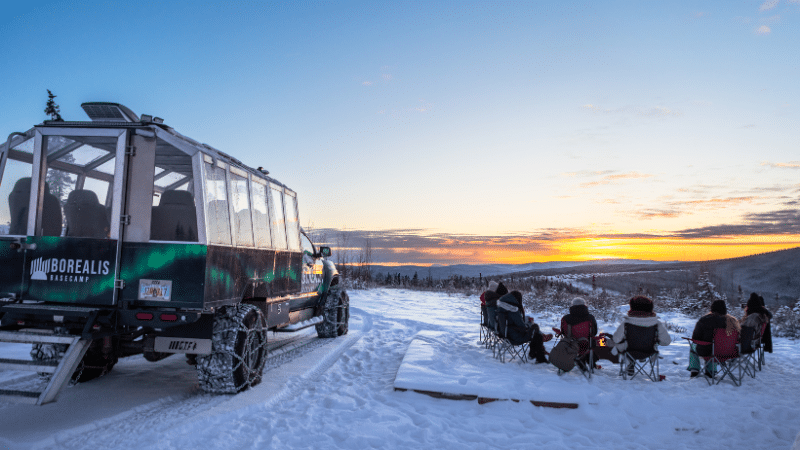 Guests enjoying a campfire as the sun sets on the snowcoach sunset tour.