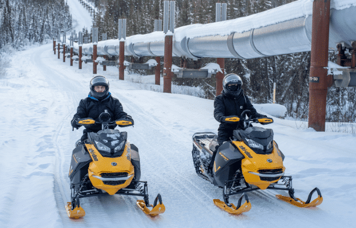 Pair of snowmobilers next to the Trans-Alaska Pipeline