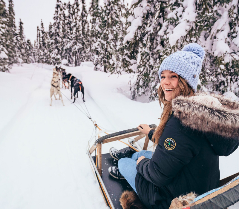 Woman on Alaskan dog sled adventure experience surrounded by snow